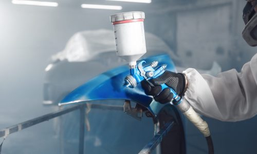 Car repair painter in protective overalls and painting a respirator part of car in the paint chamber Car repair painter in protective overalls and painting a respirator part of car in the paint chamber. Airbrush coating.